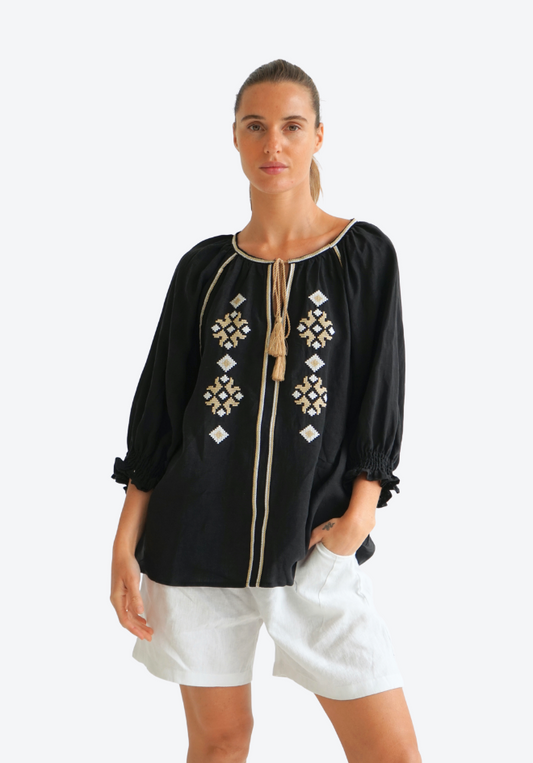 Woman wearing a black embroidered blouse with white shorts on a white background