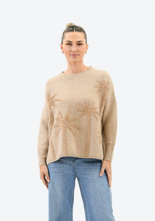 Woman wearing a beige sweater with palm tree pattern and blue jeans on a white background