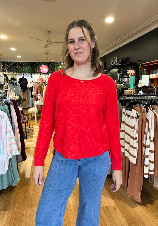 Woman wearing a red sweater and blue jeans in a clothing store.