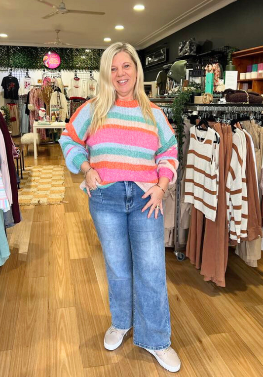 Woman wearing a colorful striped sweater and jeans in a clothing store.
