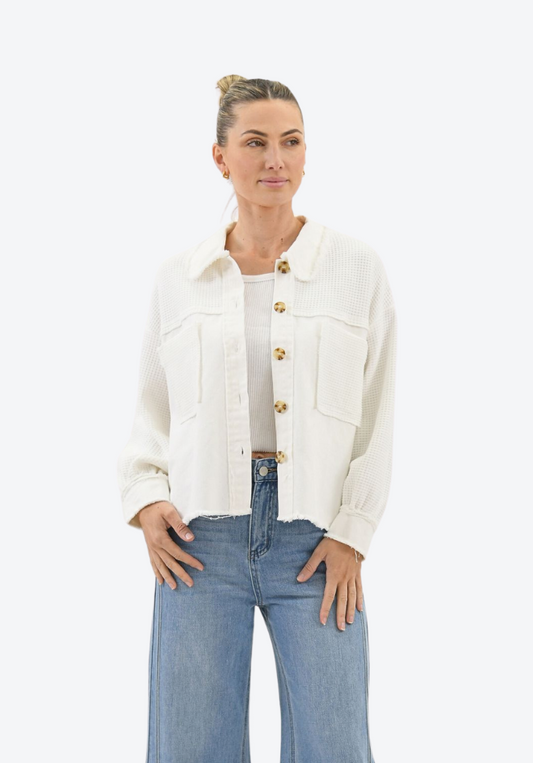 Woman wearing a white jacket with gold buttons and blue jeans on a white background