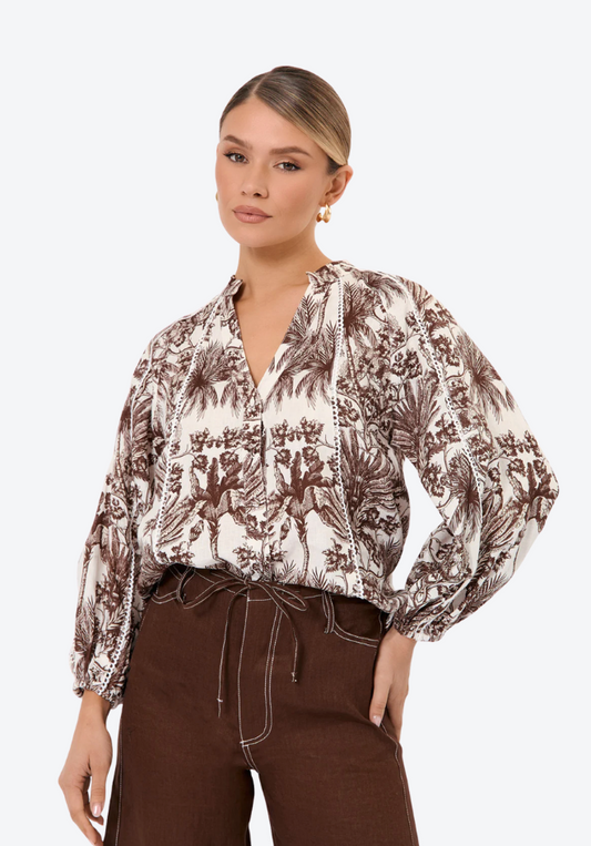 Woman wearing a patterned blouse and brown pants on a white background