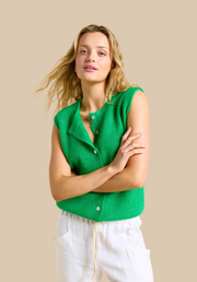 Woman wearing a green sleeveless top against a beige background