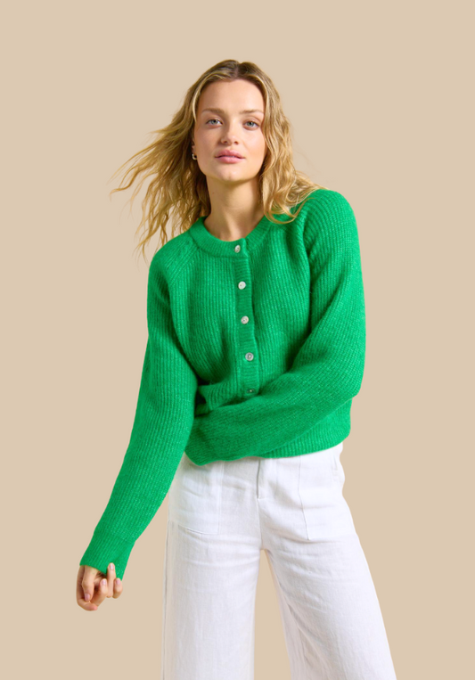 Woman wearing a green sweater and white pants against a beige background