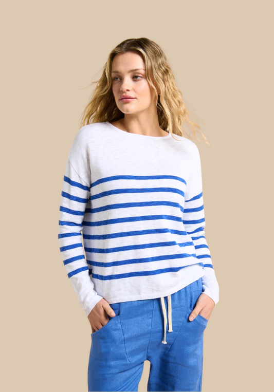 Woman wearing a white sweater with blue stripes and blue pants on a beige background