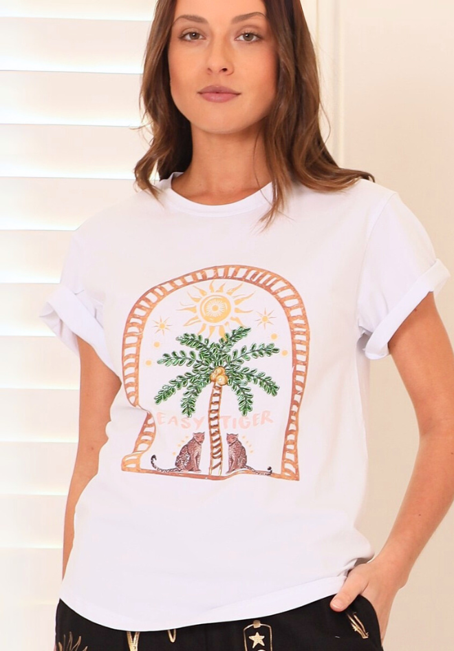 Woman wearing a white t-shirt with a palm tree and cat graphic design.