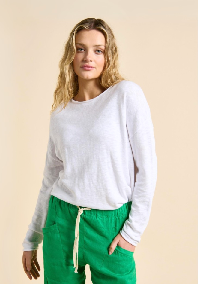 Woman wearing a white long-sleeve top and green pants against a beige background