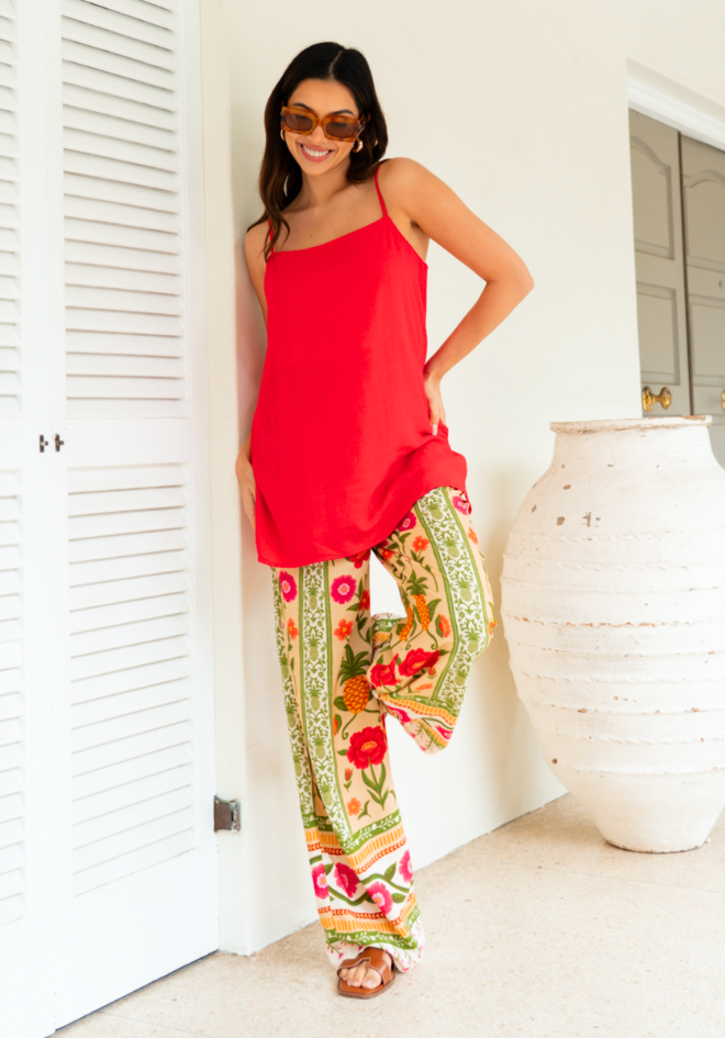 Woman wearing a red top and colorful floral pants standing in a bright room.