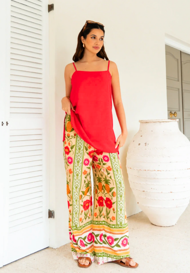 Woman wearing a red top and floral pants standing in a bright room.