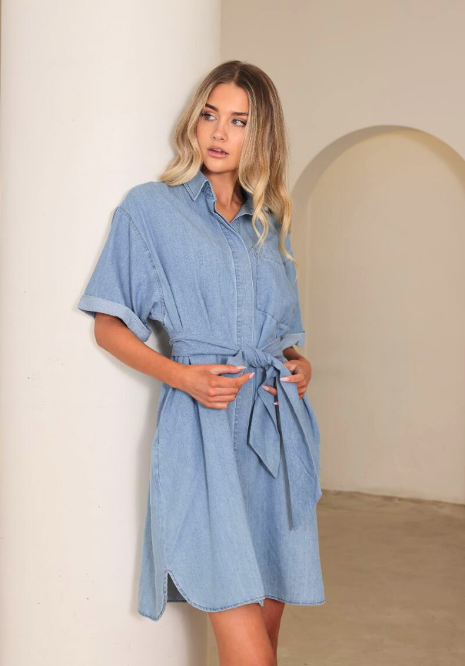 Woman wearing a light blue denim dress in a minimal indoor setting