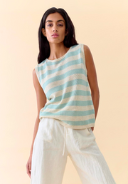 Woman wearing a sleeveless striped top and white pants against a beige background