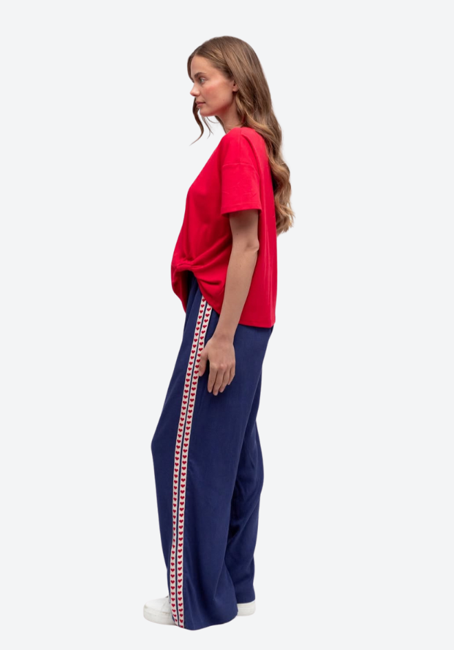 Woman wearing a red top and navy pants with a stripe, standing against a white background