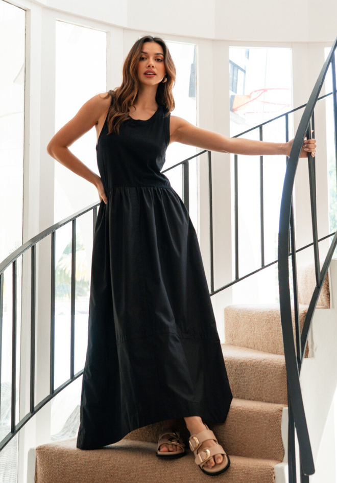 Woman in a black dress standing on a staircase with a white wall and railing in the background