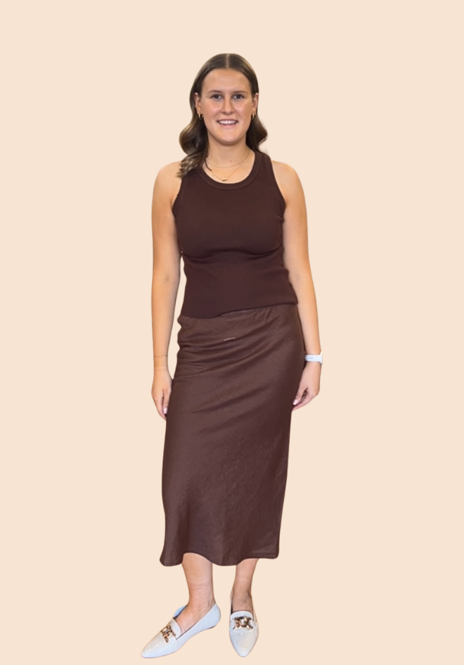 Woman wearing a brown sleeveless top and satin skirt on a beige background