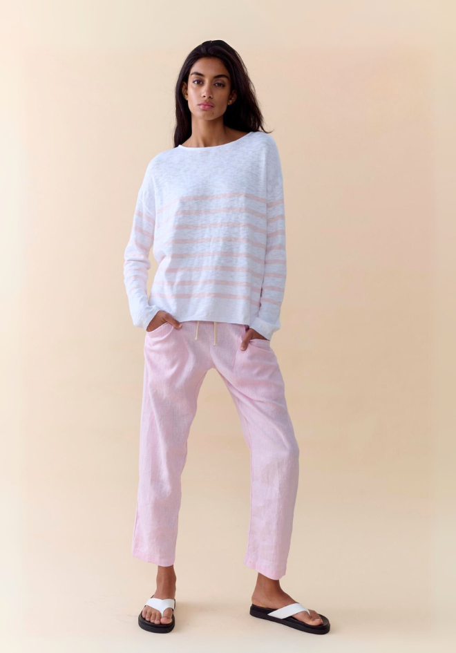 Woman wearing a light blue striped sweater and pink pants on a beige background