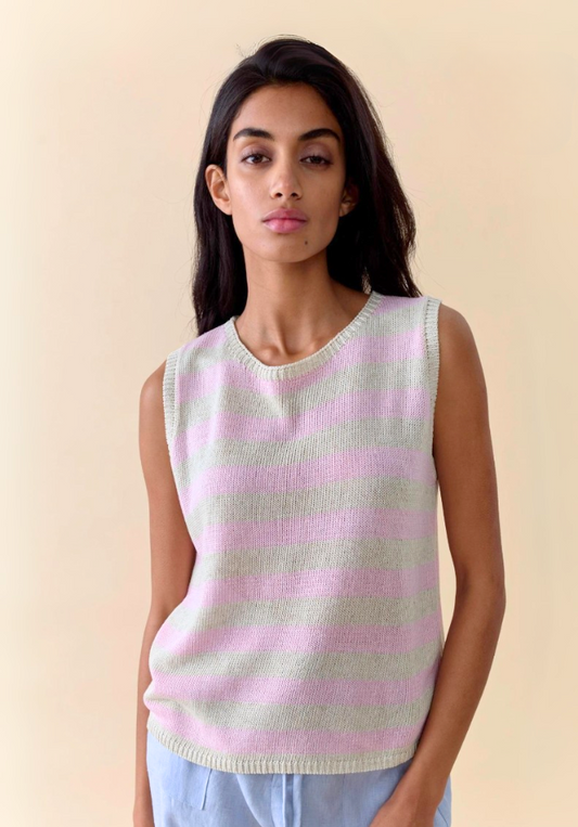Woman wearing a sleeveless pink and white striped sweater against a beige background