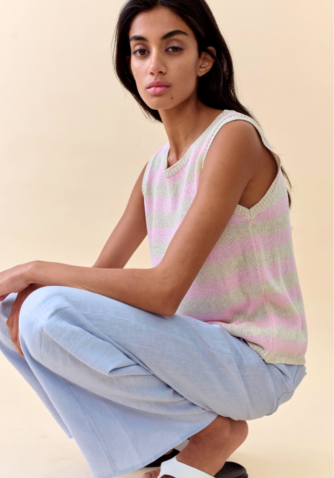 Woman wearing a striped sleeveless top and light blue pants on a beige background