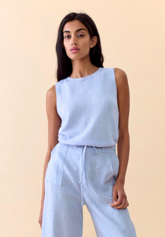 Woman wearing a light blue sleeveless top and pants on a beige background