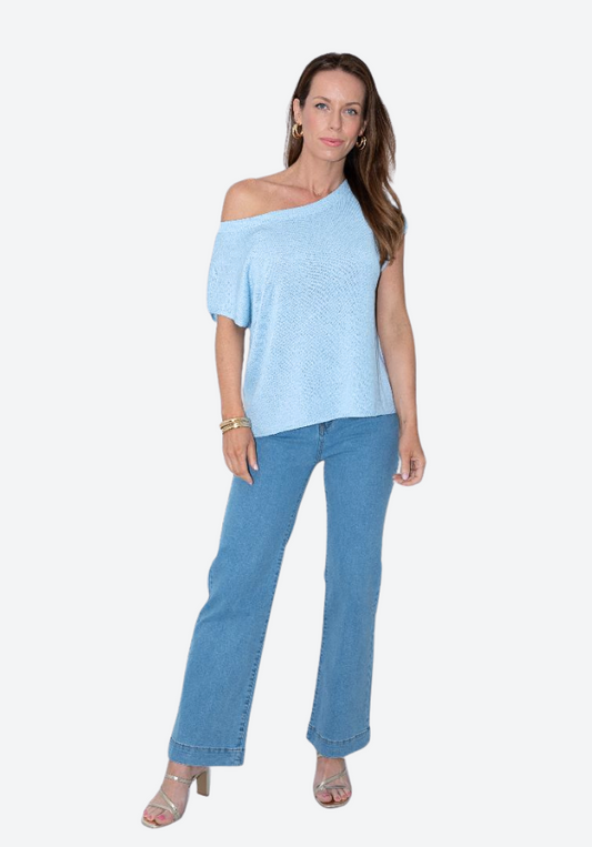 Woman wearing a light blue off-shoulder top and jeans on a white background
