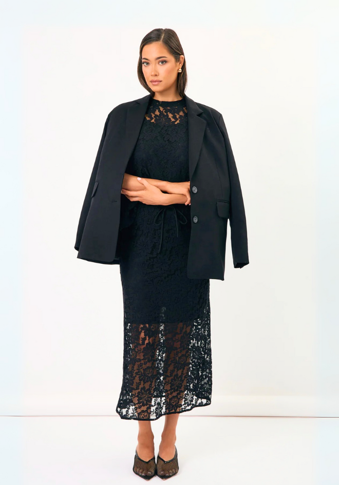 Woman wearing a black outfit with a lace dress and coat on a white background