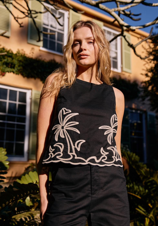 Woman wearing a black sleeveless top with white palm tree designs outdoors.