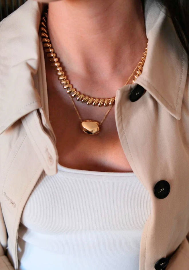 Close-up of a person wearing a beige trench coat with a gold necklace and pendant.