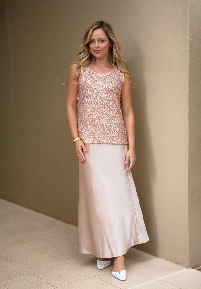 Woman wearing a sequined top and satin skirt against a beige wall.