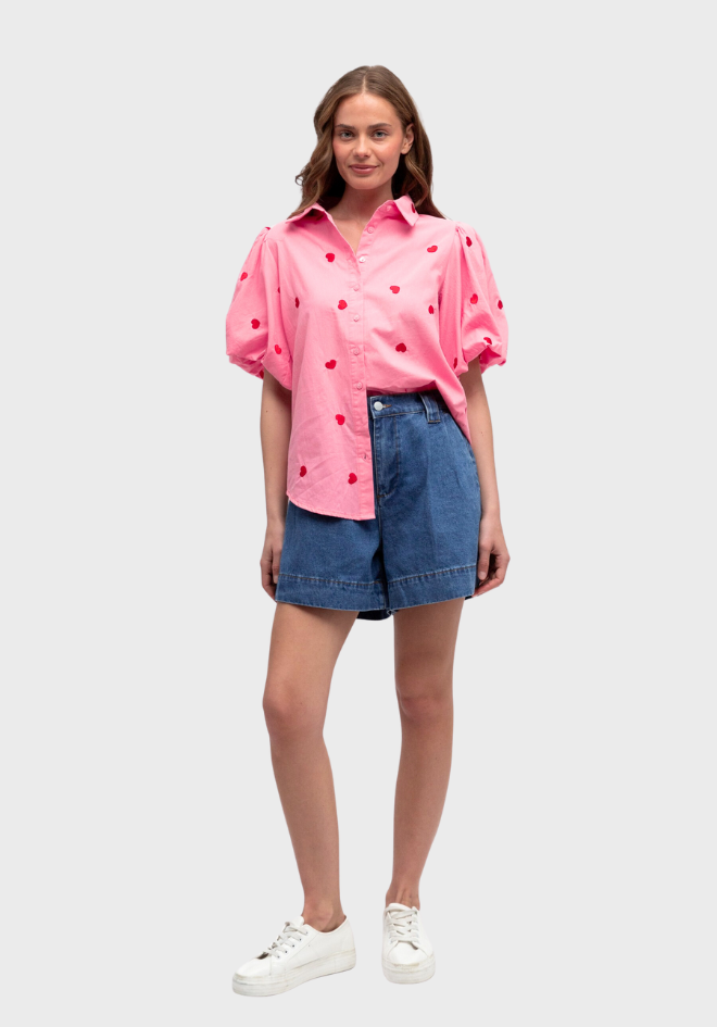 Woman wearing a pink polka dot blouse and denim shorts on a white background