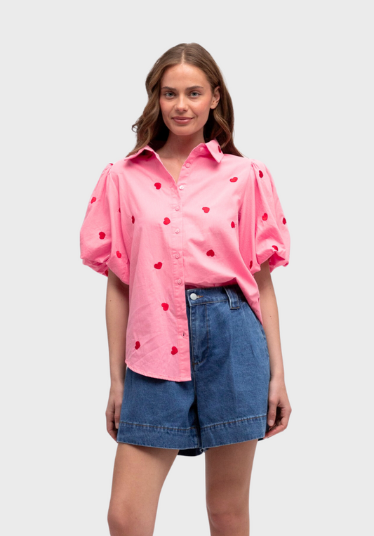 Woman wearing a pink blouse with black polka dots and denim shorts on a white background