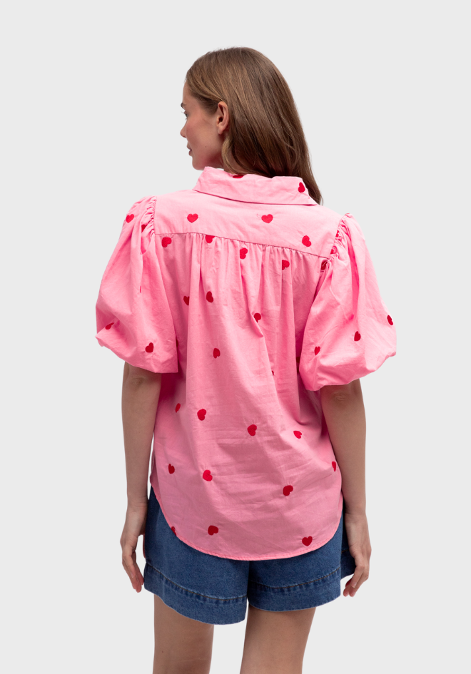 Person wearing a pink blouse with red heart patterns on a light gray background