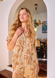 Woman wearing a beige floral-patterned outfit standing in a room with wooden furniture.