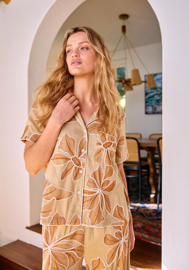 Woman wearing a beige floral-patterned outfit standing in a room with wooden furniture.