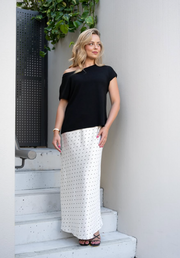 Woman wearing a black top and white polka dot skirt standing on steps with a plant in the background