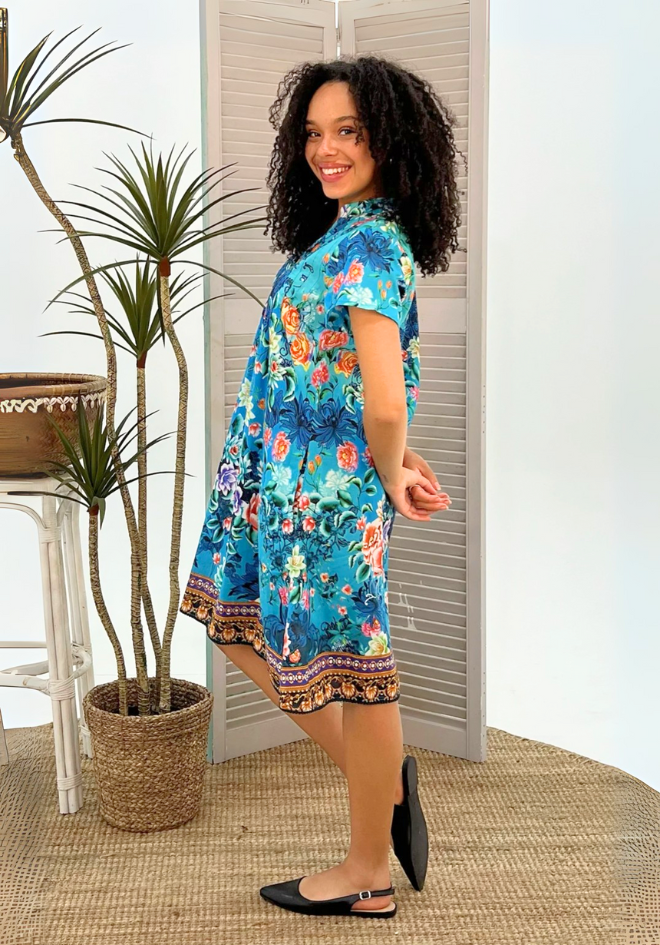 Woman wearing a colorful floral dress standing indoors with plants in the background