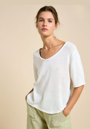 Woman wearing a white sweater and green pants against a beige background