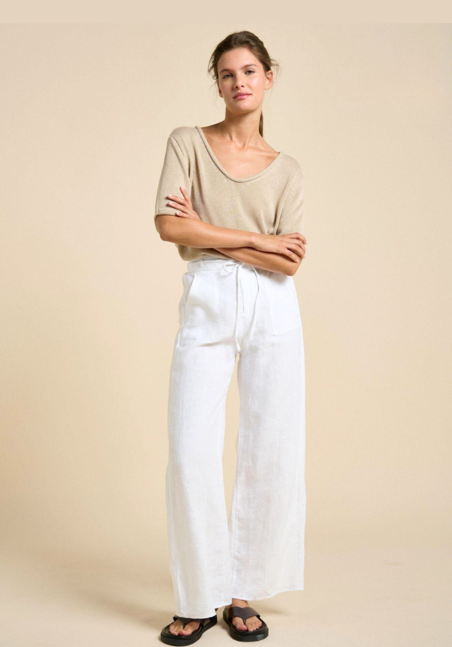 Woman wearing a beige top and white pants against a beige background