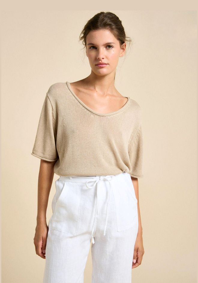 Woman wearing a beige top and white pants against a beige background