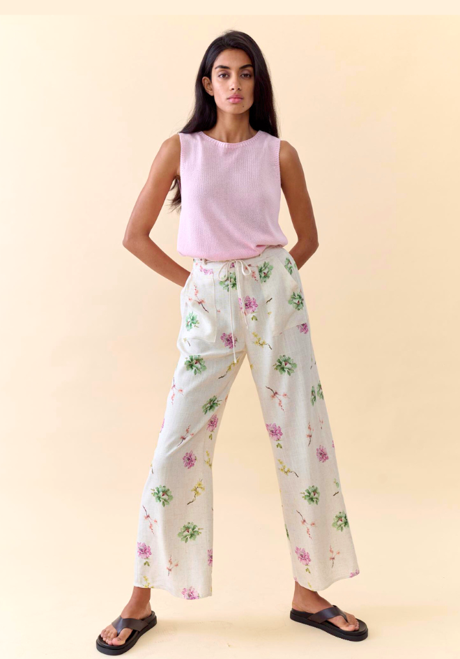 Woman wearing a light pink sleeveless top and floral pants on a beige background