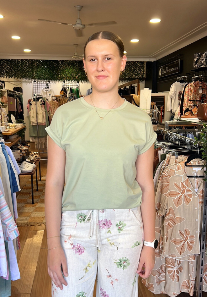 Woman standing in a clothing store wearing a light green top and floral pants.