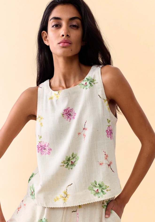Woman wearing a white sleeveless top with floral patterns on a beige background