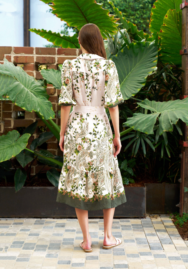 Woman wearing a floral dress standing in a garden with large green leaves.