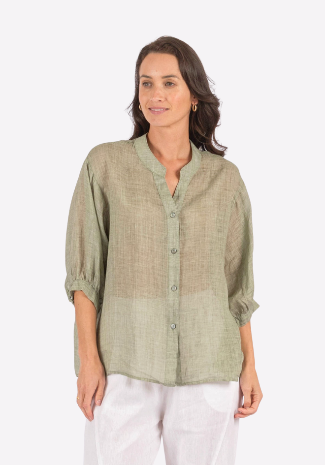 Woman wearing a green button-up shirt and white pants on a white background