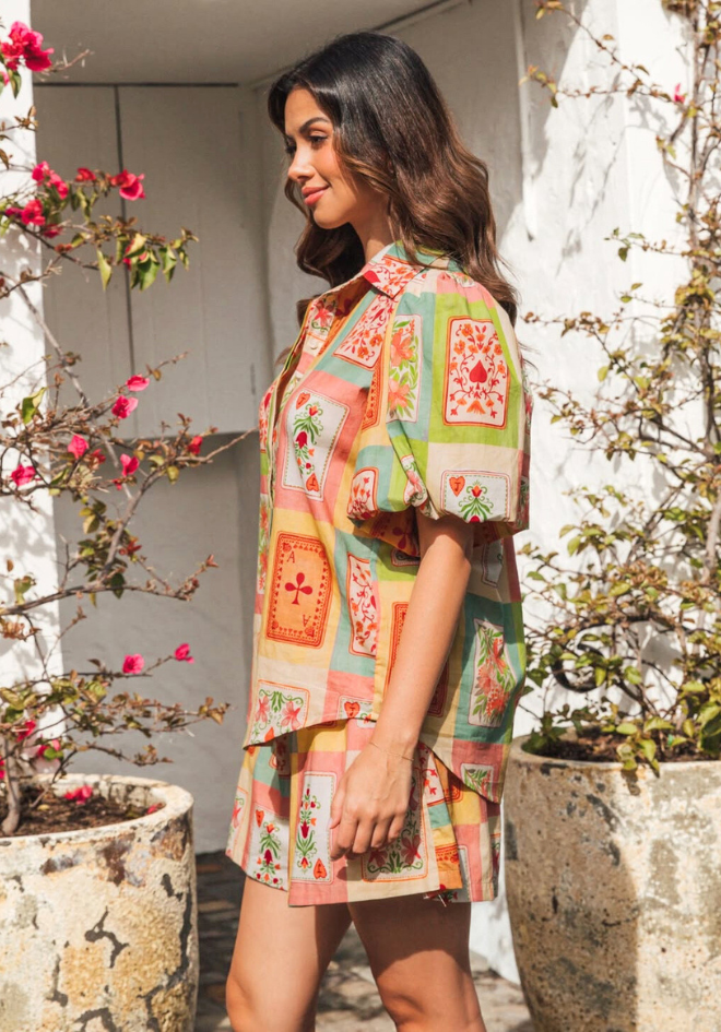 Woman wearing a colorful patterned dress standing outdoors with plants and flowers.
