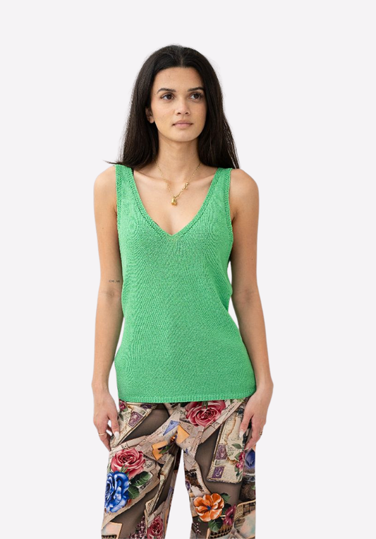 Woman wearing a green sleeveless top with floral pants on a white background