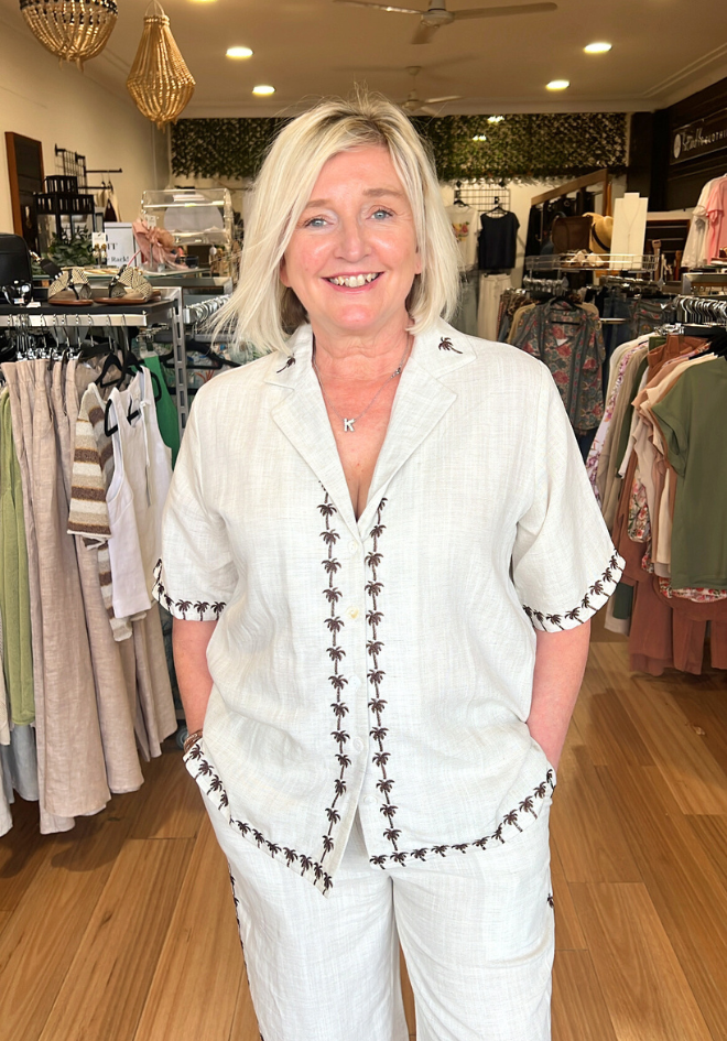 Woman in a white outfit with black trim standing in a clothing store.