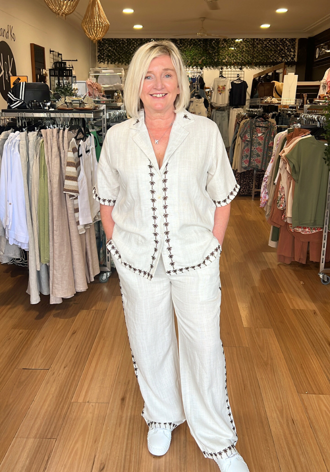 Woman in a white outfit standing in a clothing store with racks of clothes in the background.