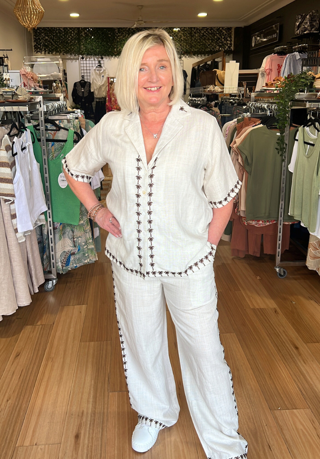 Woman in a white outfit with decorative trim standing in a clothing store.