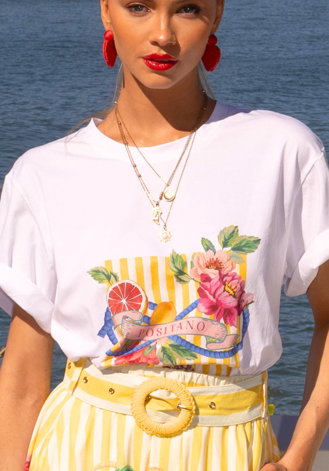 Woman wearing a white t-shirt with colorful graphic design and yellow striped pants by the water.