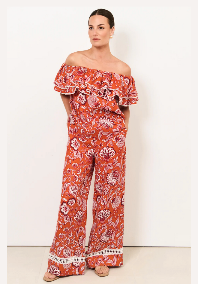 Woman wearing a red floral off-shoulder top and wide-leg pants on a white background