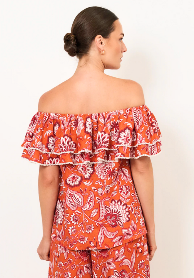 Woman wearing an orange floral off-shoulder top and pants on a white background